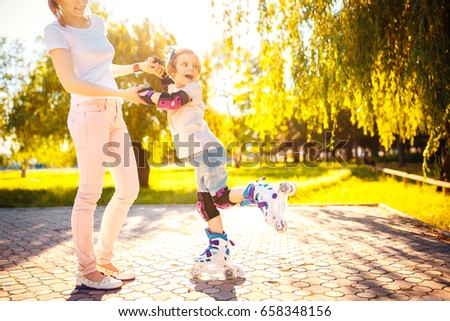 Horizontal outdoors shot of woman helping daughter to ride roller skate in park in sunny day.