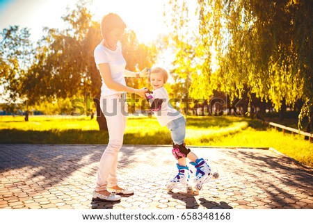 Horizontal outdoors shot of woman helping daughter to ride roller skate in park in sunny day.