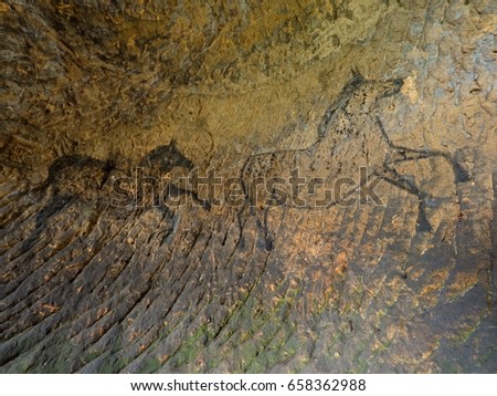 Discovery of prehistoric paint of horse in sandstone cave. Spotlight shines on historical human painting. Black carbon horses on sandstone wall. Paint of hunting,  prehistoric picture