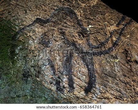  Black carbon mammoth on sandstone wall. Paint of human hunting,  prehistoric picture. Discovery of human history. Prehistoric art of mammoth in sandstone cave. Spotlight shines on historical painting