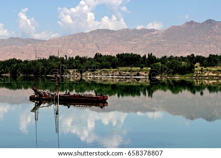 GUIDE, CHINA - JUNE 27, 2011: A red metal boat sits peacefully on the Yellow River in the middle of a mirror-like reflection of the blue sky with scattered clouds