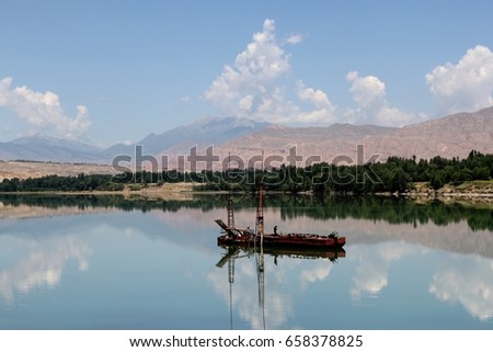 GUIDE, CHINA - JUNE 27, 2011: A red metal boat sits peacefully on the Yellow River in the middle of a mirror-like reflection of the blue sky with scattered clouds