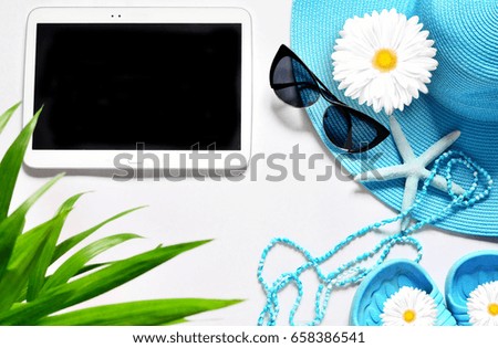 Summer concept. Tablet with black screen on white surface with summer beach items, top view.