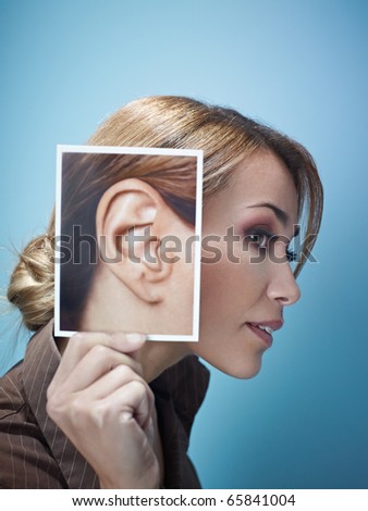 mid adult business woman holding photo of her ear on blue background. Vertical shape, side view, head and shoulders, copy space Royalty-Free Stock Photo #65841004