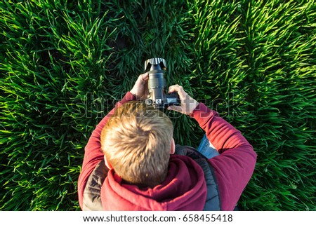 fascinating photography and process of shooting concept - top view of young male man with mirror camera in hands standing in a field of bright green grass, jeans and jacket hoodie