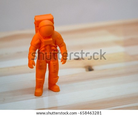 The model printed on a 3d printer. The object in the form of an orange cosmonaut is on the table. Progressive modern additive technology. Copy spase, spase for text.