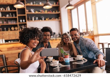 Multiracial people having fun at cafe taking a selfie with mobile phone. Group of young friends sitting at restaurant taking self portrait with smart phone.