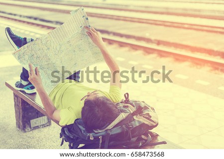 Handsome man lying on the backpack and look at the map comfortably.While waiting to travel at the train station,mage for travel and freedom life concept