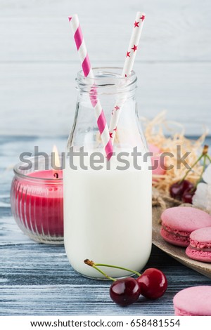 Bottle of milk with pink french macaroons, striped straw, lit candle, peony flower