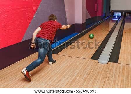 close up of young man in checkered shirt throwing ball to alley in bowling club, leisure and sport concept