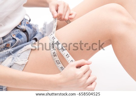 Close up of female hands using measuring tape measuring her legs size (healthy and weight loss or diet concept) isolated on white background