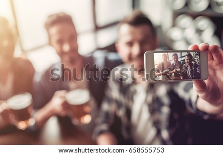 Handsome men in bar are drinking beer and taking selfie.