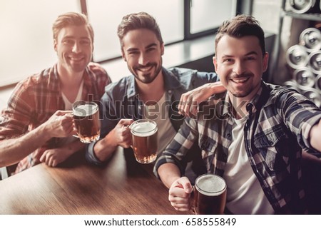 Handsome men in bar are drinking beer and taking selfie.
