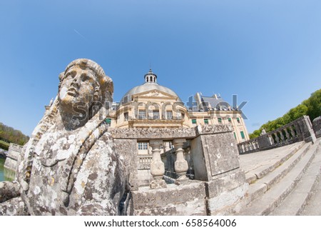 A Beautiful Rock Statue With The Chateau De Vaux Le Vicomte In The Background. The House Is A Baroque French Chateau Located In Maincy, Near Melun, 55 Km Southeast Of Paris Taken With Fisheye Lens.