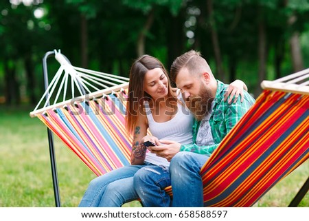 Young couple with mobile phone sitting on hammock