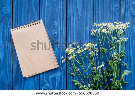female desktop decoration with flowers and notebook on blue wooden background top view mock-up