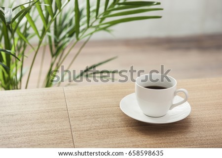 A coffee cup with green plant on the wood desk.