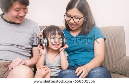 Asian parents and baby girl in sofa using tablet and headphones
