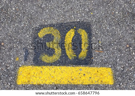 Yellow imprint of the number thirty on a tarmac road.
