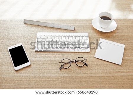 A smart phone with keyboard, coffee, pad, glasses, ruler on the wood desk.