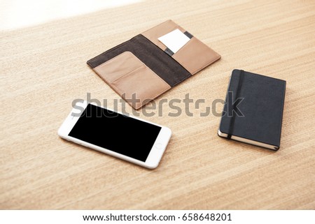 A smart phone with wallet, glasses, note on the wood desk.