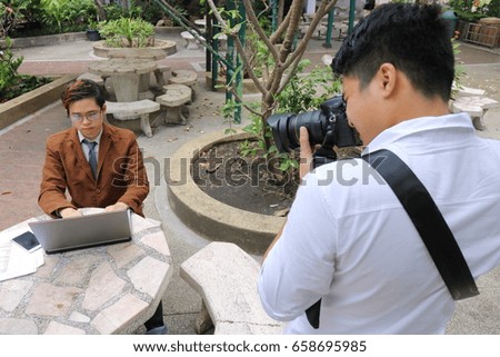 Photographer takes a photo of portrait of handsome young business man while using laptop.
