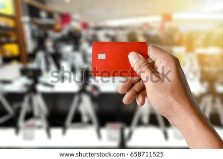 a hand holding credit card on blurred camera shop store, modern life shopping concept