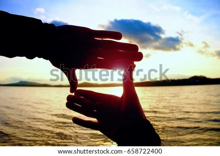 Holding hands in square shape with sun immersing at the horizon 