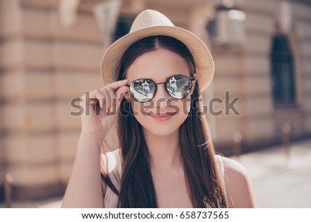 Close up of young cute smiling girl in mirror sunglasses and hat at the vacation, walkimg in the city outdoors. She is happy, fixing her eyewear Royalty-Free Stock Photo #658737565