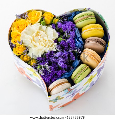 box in the shape of a heart with purple, yellow and white flowers and macaroons, flat lay
