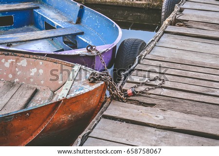 Old iron frayed and shabby boat noses tied to wooden dock close-up