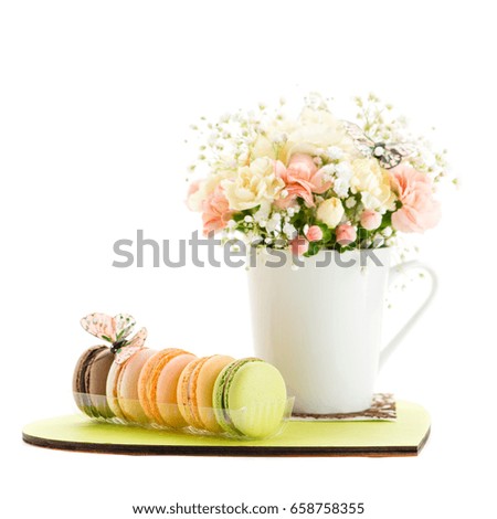 pastel flowers in a white cup and macaroons on a plate in the shape of heart. Isolated on white background
