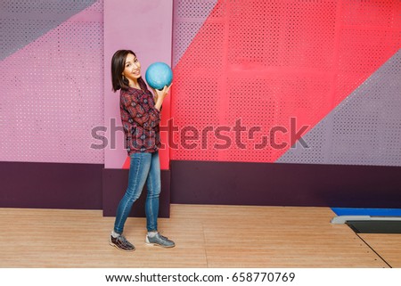 Beautiful young asian woman holding bowling ball and looking at the camera.