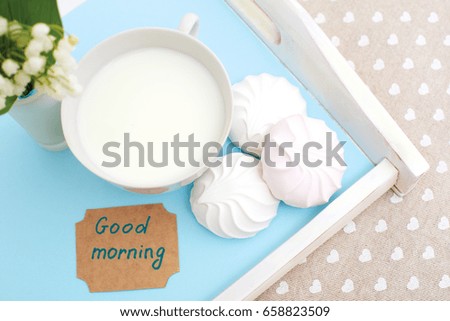 A mug of milk, marshmallows and flowers lie on a blue wooden tray. Healthy breakfast