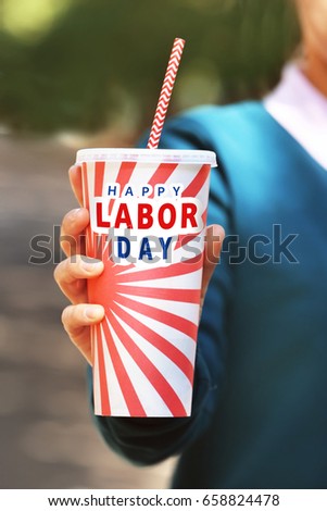 Woman holding paper cup with text HAPPY LABOUR DAY outdoor, closeup