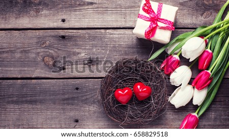 Decorative red little hearts  in nest, bright  spring  tulips flowers, box with present  on textured background.  Selective focus. Place for text. Toned image.
