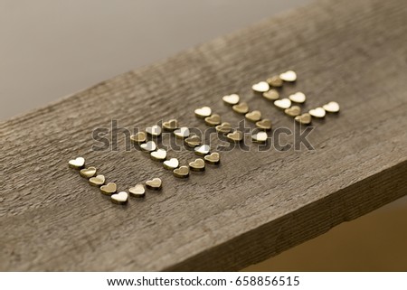 Golden hearts placed in shape of word Love on wooden background captured with shallow depth of field