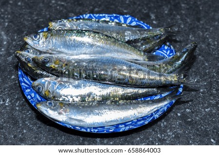 Dish with raw sardines, on black marble background
