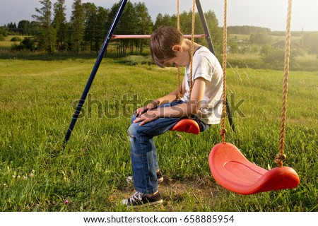 Sad lonely boy sitting on swing alone Royalty-Free Stock Photo #658885954