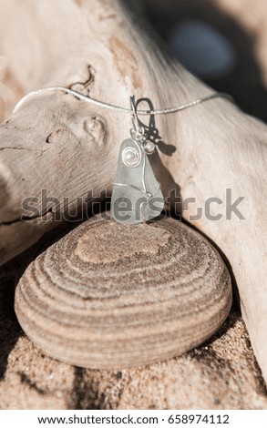 Unique handmade clear sea glass jewellery, with a silver chain on a rustic sand and driftwood background