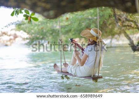 Beautiful woman playing ukulele under a tree by the sea.