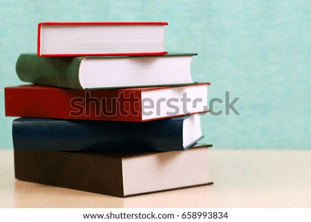Open book, stack of hardback books on wooden table.