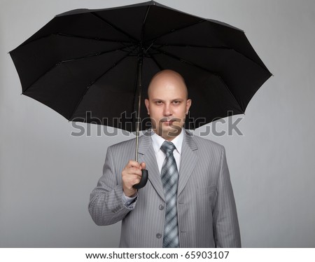 Bald businessman in a gray suit with a gray background with a black umbrella in hand