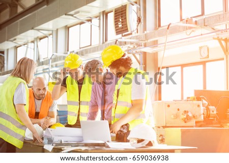 Male architect and manual workers discussing over blueprints in industry