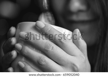 Black and white image of Asian woman holding and looking at hot coffee with smiley face