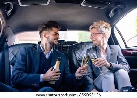 Business woman and business man are toasting with champagne in limousine, for success