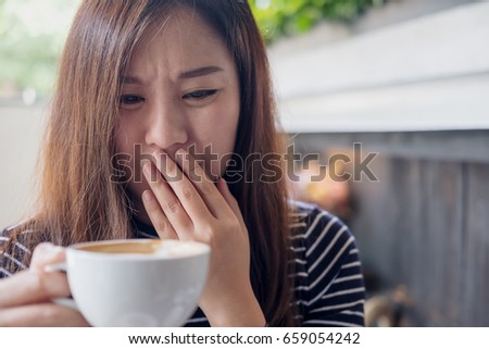 Closeup image of Asian woman holding hot coffee with feeling strange and smelling bad in coffee shop