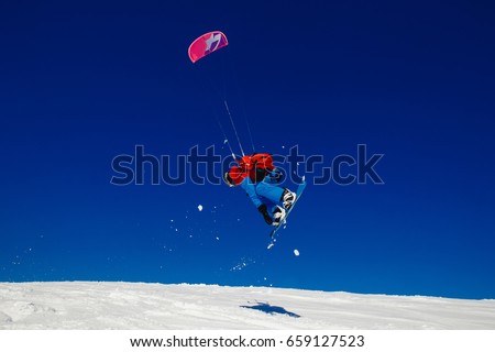 Snowboarder with kite jump on fresh snow in winter in tundra against clear blue sky. Concept sports snowkite. Royalty-Free Stock Photo #659127523