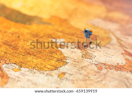 Miniature people, travelers with backpack standing on world map, walking to destination