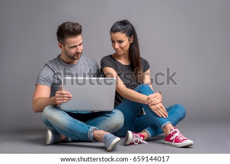 A beautiful young couple sitting on the ground and looking at a laptop and smiling
